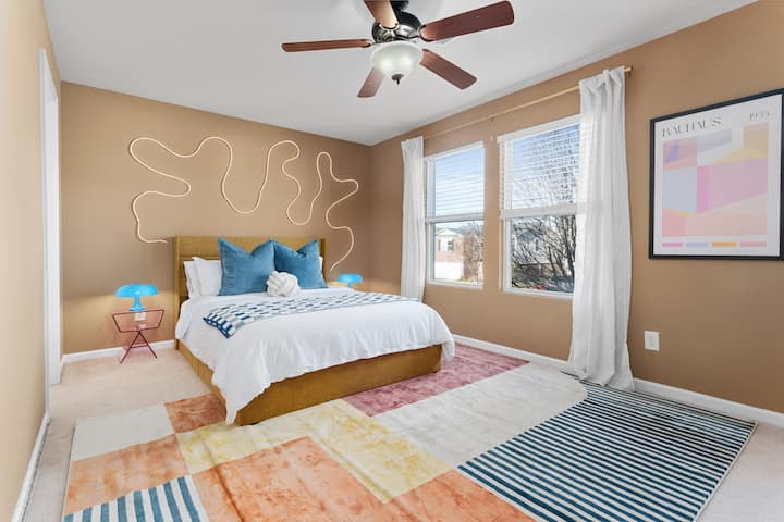 Relájate en el ambiente sereno de este dormitorio con una lujosa cama tamaño queen, un suave ventilador de techo en la parte superior y ventanas adornadas con cortinas que invitan a una luz suave y natural.