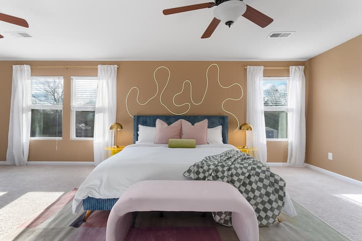 Relájate en la amplia serenidad de este gran dormitorio adornado con dos elegantes ventiladores de techo, una majestuosa cama tamaño king y luz solar que se filtra suavemente a través de las cortinas transparentes.