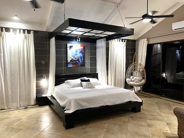 Დიდი ზომის საწოლი უზარმაზარ საძინებელში.  Ასევე, წარმოდგენილია კვერცხის სტილის საქანელა სკამი ოკეანის ხედებით.