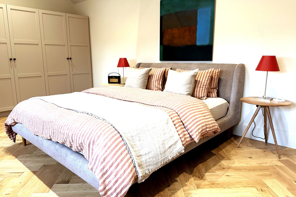 Een ruime slaapkamer met super kingsize bed; ganzendons kussens en dekbed en biologisch beddengoed; Roberts radio aan het bed. De ramen kijken uit op de ommuurde privétuin.  Er is veel hangruimte in speciaal gebouwde kasten. 