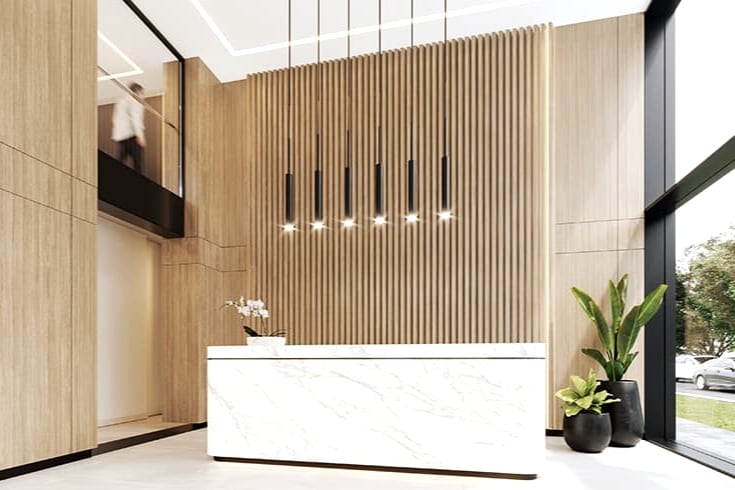 The entryway features a sleek reception desk with a marble finish, complemented by vertical wooden paneling. Modern pendant lights hang above the desk, casting a warm glow. Potted greenery is present, adding a natural element to the stylish space.