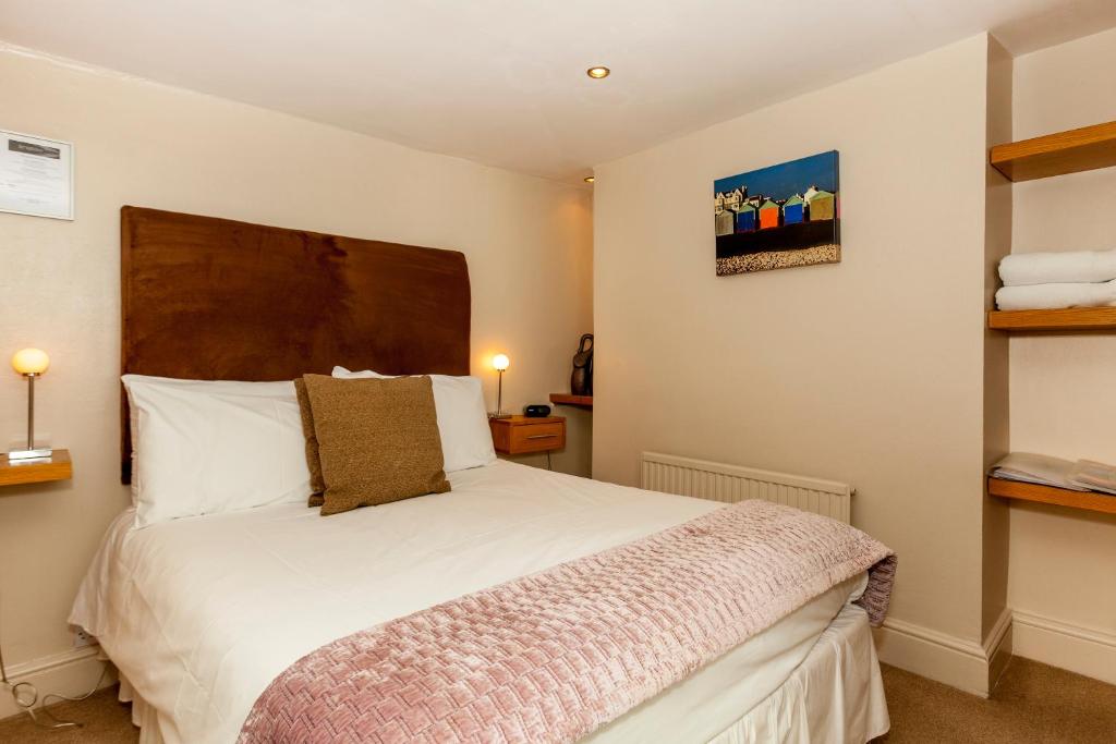 A cozy room featuring a double bed centered against a wooden headboard. Soft lighting is provided by bedside lamps on either side. A colorful artwork adorns the wall above shelves displaying neatly stacked towels, contributing to a functional and comfortable space.