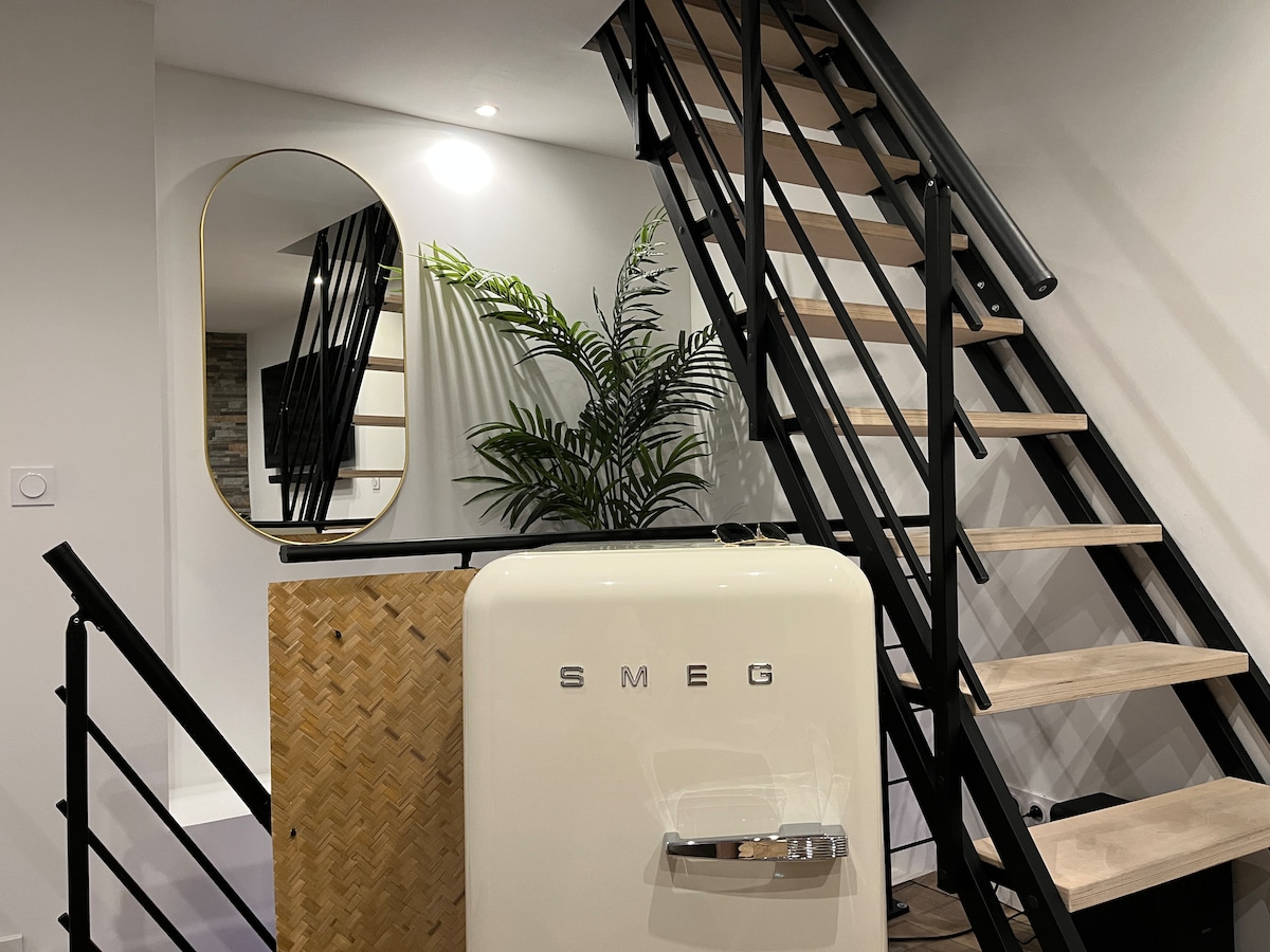A stylish staircase with wooden steps leads to the upper level. A vintage SMEG refrigerator stands prominently, complementing a decorative mirror with an oval shape. A green plant provides a touch of nature, contributing to the overall modern design of the space.