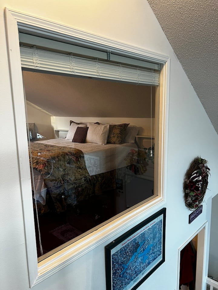 Прозорец од главната спална соба, со отворени ролетни, со поглед кон езерото. 