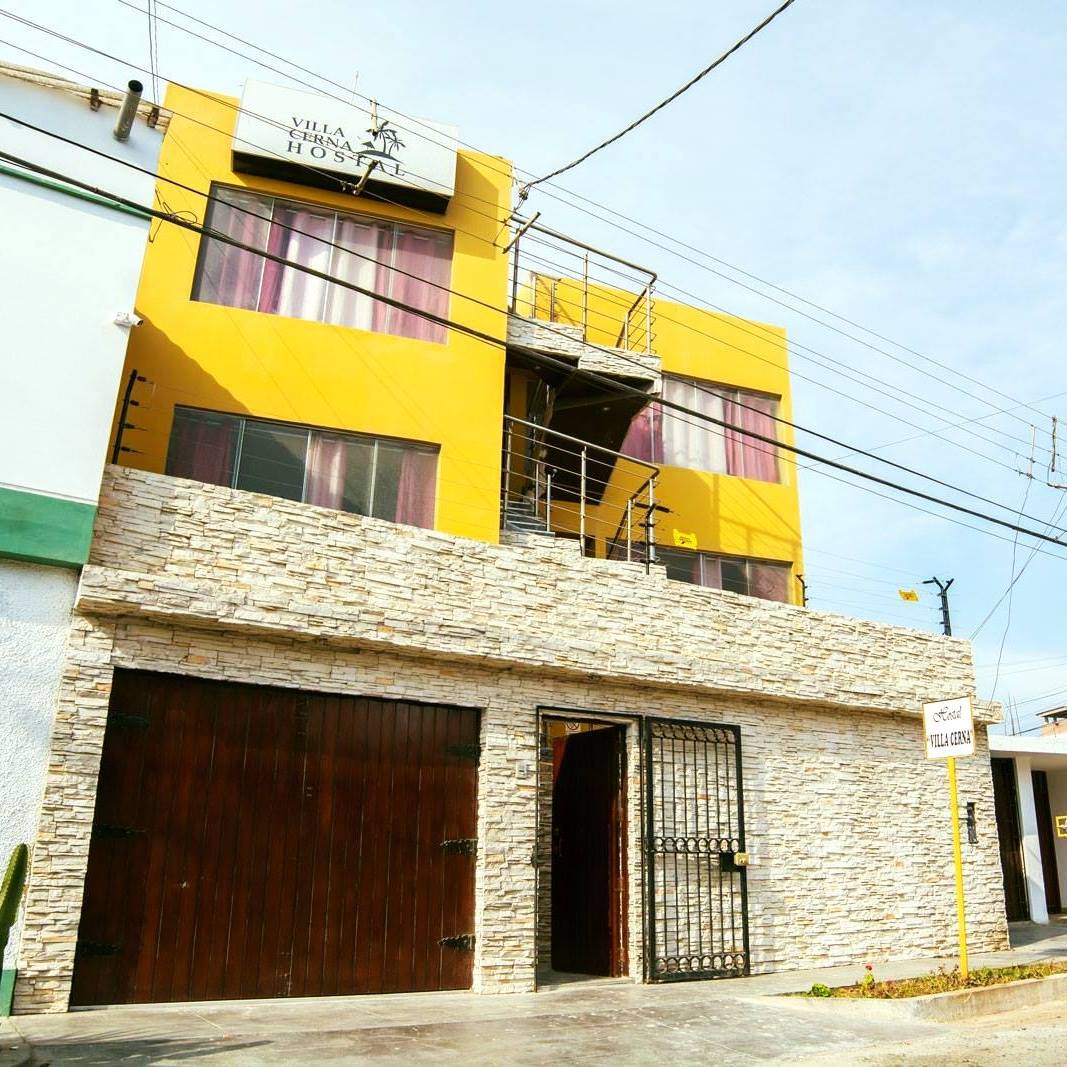 A three-story building is featured, highlighted by yellow exterior walls. Large windows with purple curtains provide natural light to the interior. The stone-clad lower level adds texture, while a gated entrance leads to the enclosed parking area.