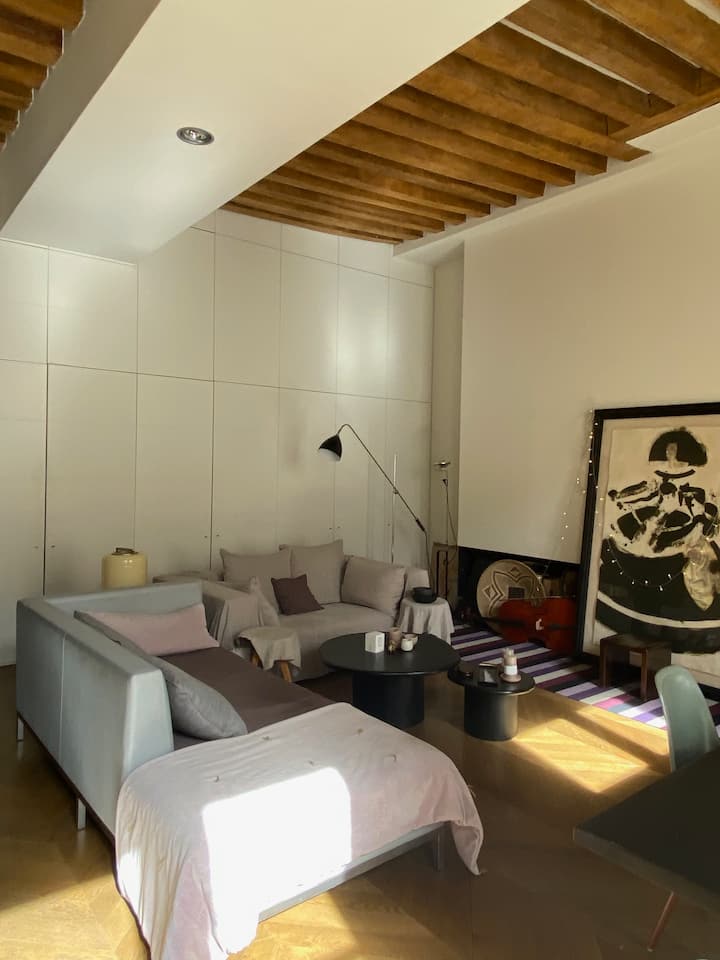 
Sala de estar con un sofá de ropa de cama y un meridiano para 3 mesas, 2 mesas de centro, luz de BTC london y FLOS, pintura y cesta africana. Suelo de madera y techo de vigas de madera. El encanto de un antiguo edificio con una renovación contemporánea.