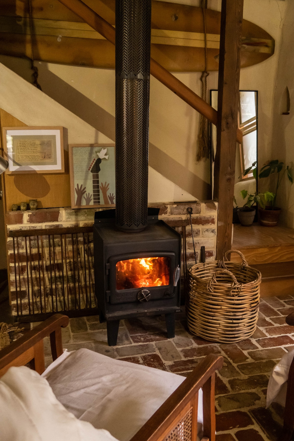 A wood fire stove is centrally located in the cozy living area, providing warmth and comfort. The stove is complemented by a rustic brick surround and wooden accents. Nearby, a woven basket adds a touch of natural texture to the space.