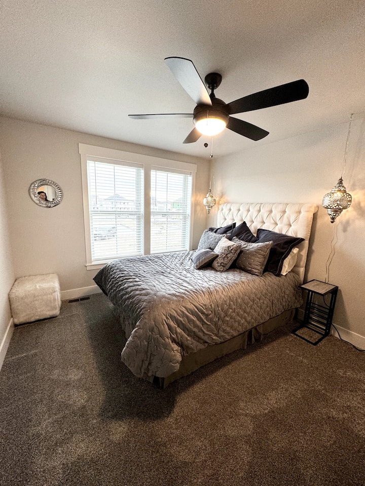 Väčšia spálňa s matracom Queen, dvoma nočnými stolíkmi, stropnými ventilátormi a komodou so zrkadlom. 