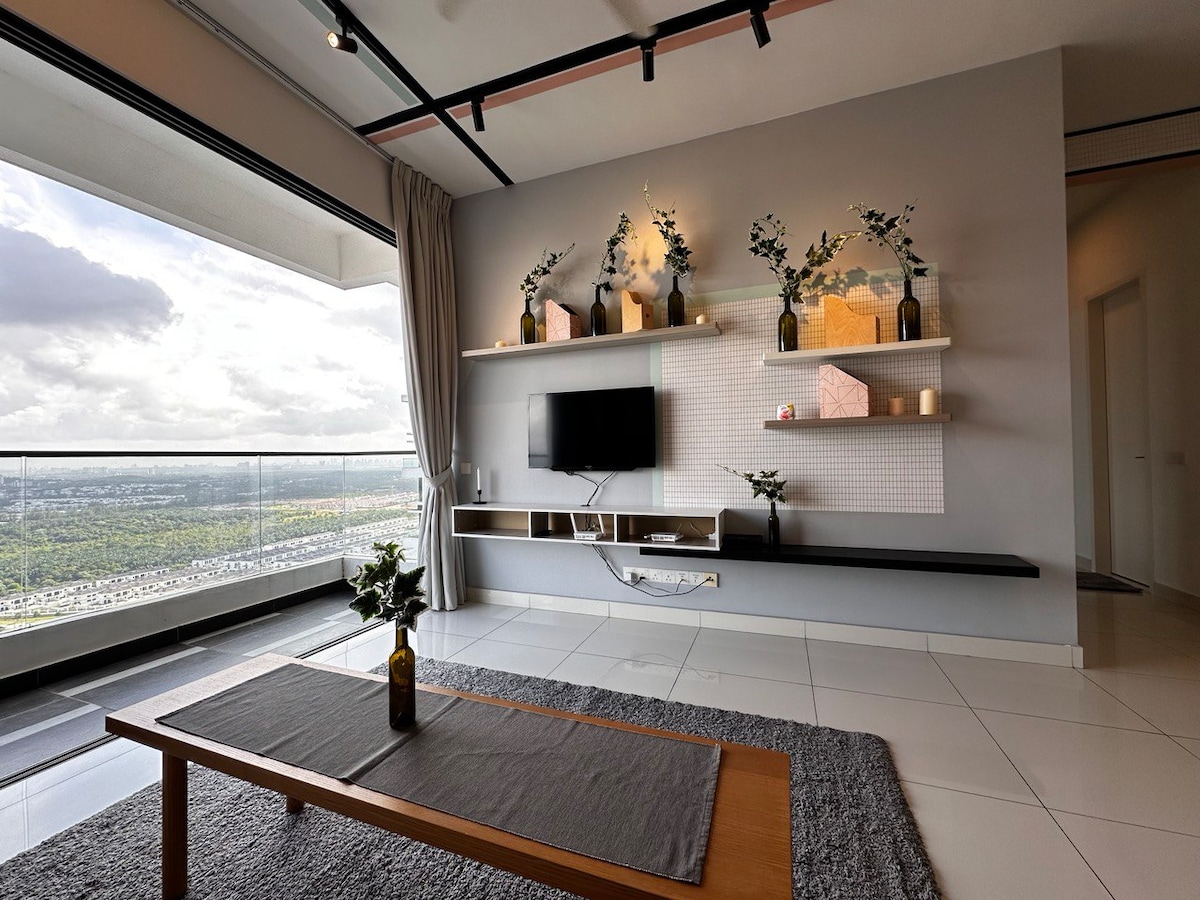 A modern living area features a sleek flat-screen TV mounted on a stylish wall shelf, accented by decorative vases and framed items. A minimalistic coffee table is placed on a soft area rug, with large windows allowing natural light to fill the space and offering expansive views.