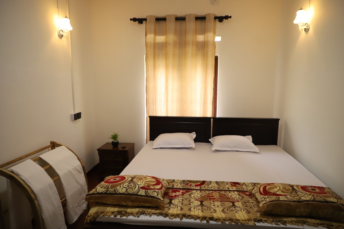 A comfortable sleeping area is highlighted by a spacious bed with white bedding and two pillows. A decorative throw lies at the foot of the bed. Soft lighting is provided by wall sconces, and a curtain partially covers a window beside the bed.