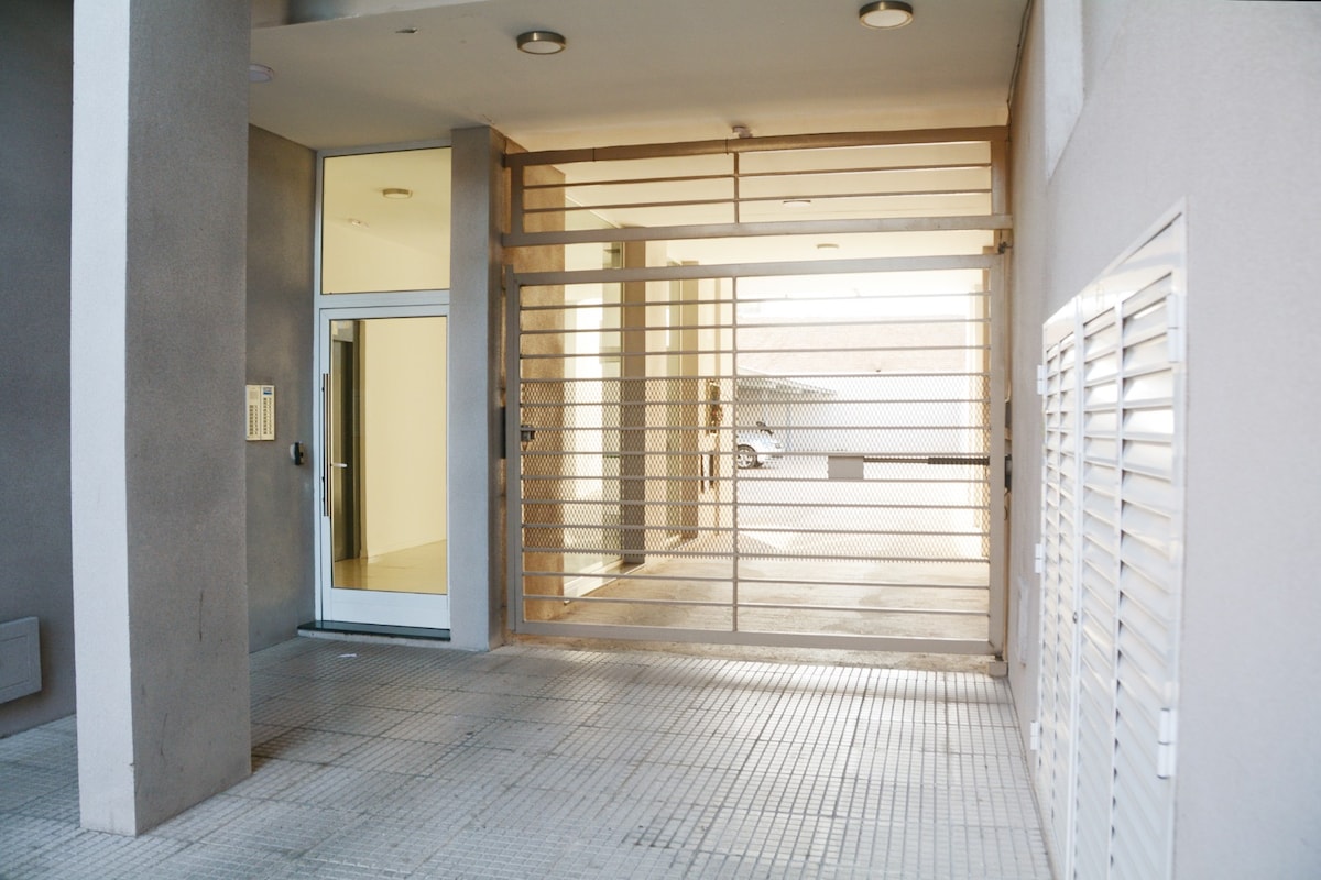 An entryway is visible, featuring an open gate that leads to a light-filled pathway. The entrance is bordered by smooth concrete walls, with a secure door to the left. Subtle lighting overhead enhances visibility of the surrounding area.