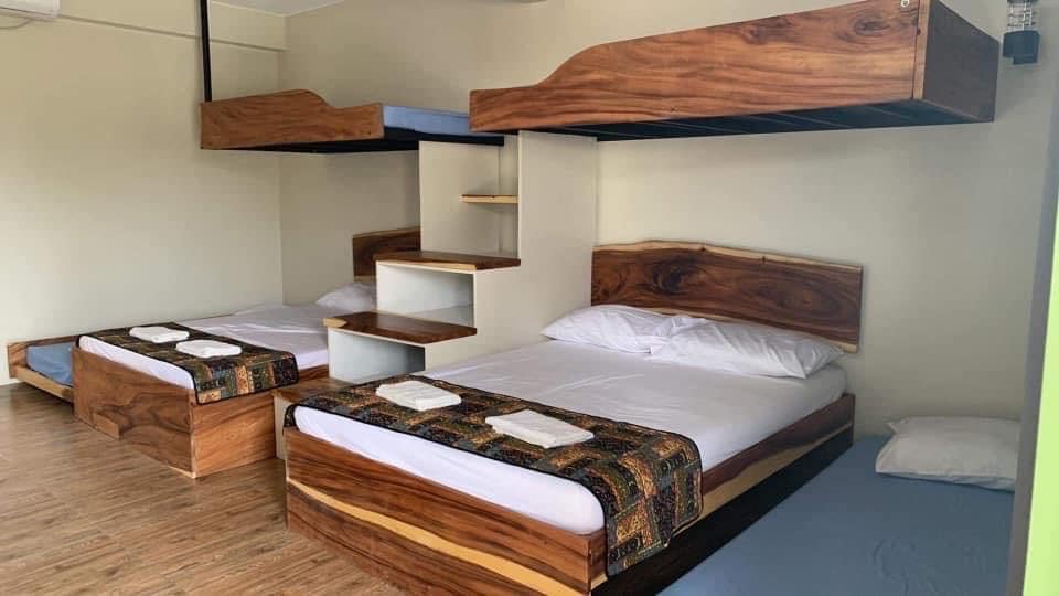 The room features two spacious beds with wooden frames, one of which is elevated with a bunk layout. Soft linens and neatly folded towels are arranged on each bed. A small shelving unit is positioned against the wall, contributing to the room's functional design.