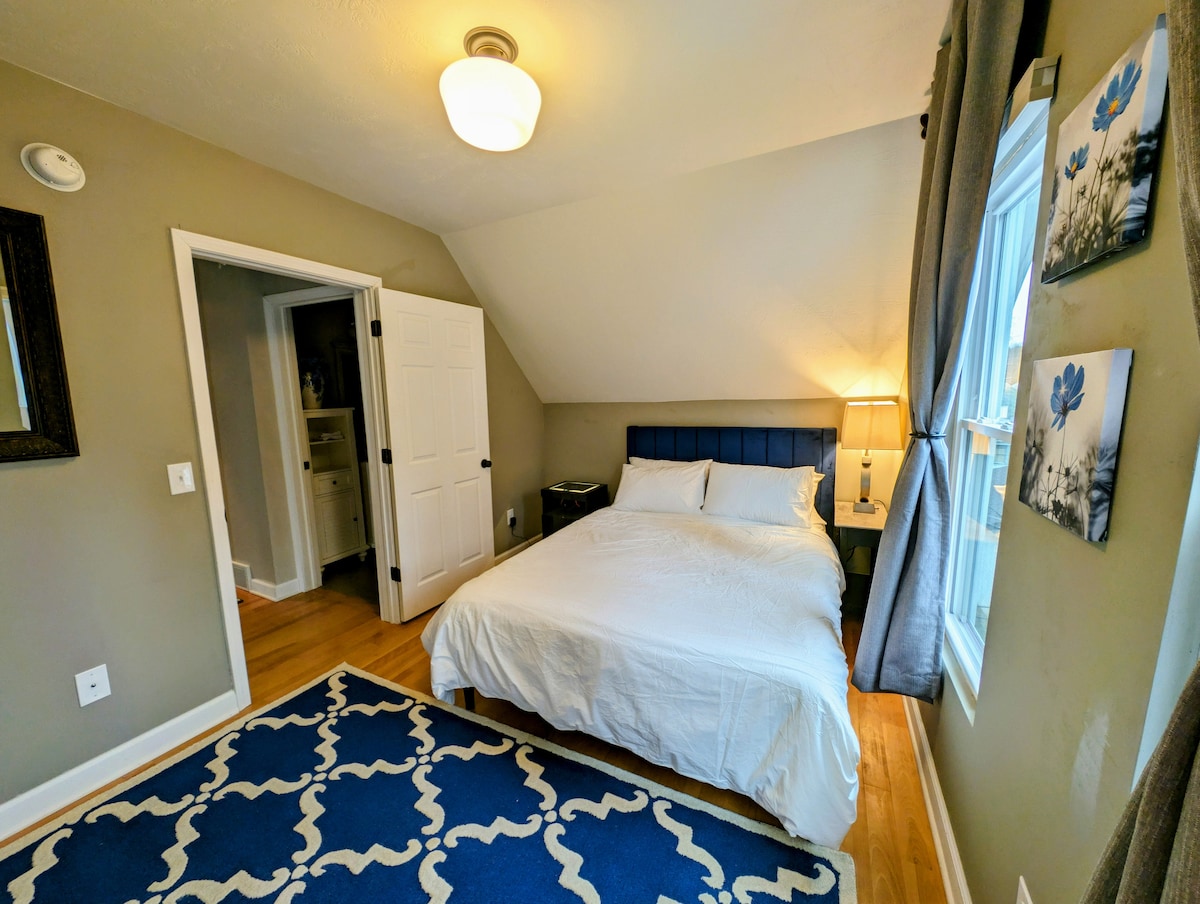 标准双人床卧室。较小的床头柜顶部可折叠，配有USB-A插头和插座（灯目前插入插座）。  较大的床头柜内置灯光和无线充电。