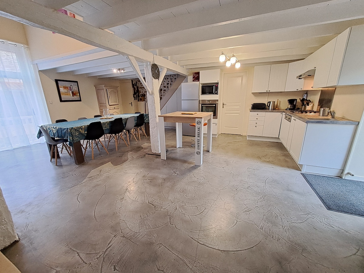 A spacious open-plan kitchen and dining area features modern appliances and ample seating. A dining table is set to accommodate several guests, while the kitchen is equipped with sleek cabinetry and a central island. Natural light fills the space through large windows.