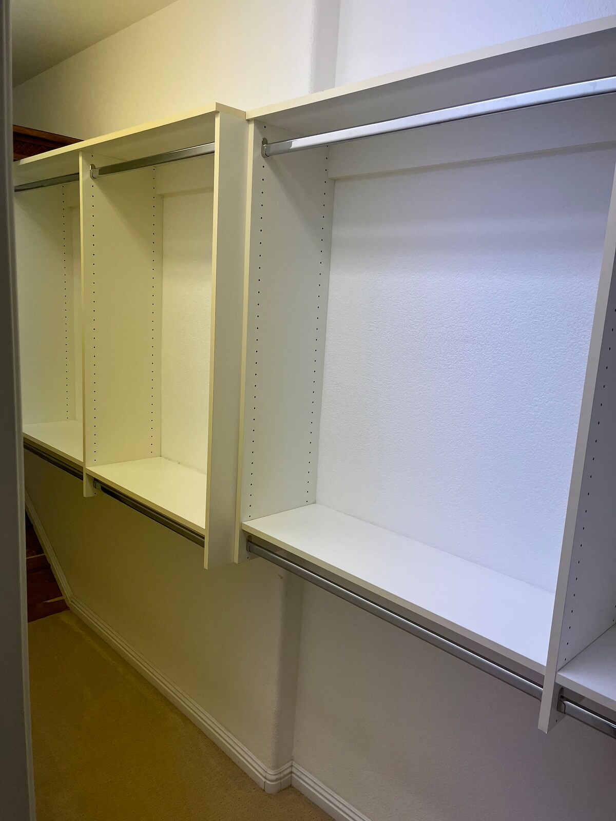 A walk-in closet with multiple open shelves is displayed, featuring a clean, minimalist design. The smooth white surfaces and ample space suggest a perfect area for organizing belongings. Soft lighting brightens the area, highlighting the uncluttered layout.