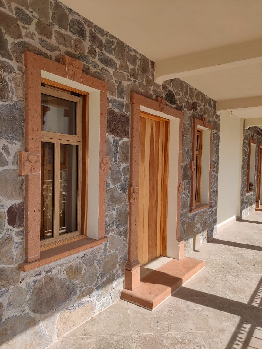 A corridor features natural stone walls, highlighted by decorative stone trims around the windows and doors. Sunlight creates light and shadows on the smooth floor, enhancing the spaciousness of the area.