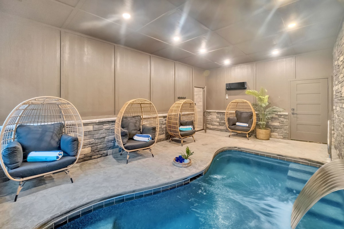 An indoor pool area is highlighted by a private heated swimming pool surrounded by a smooth stone wall. Comfortable hanging chairs with plush cushions provide space for relaxation, while a small plant adds a touch of greenery to the tranquil setting.