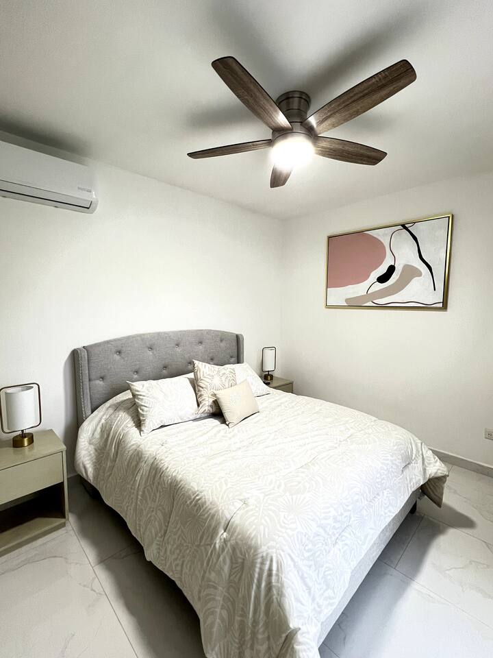 Grande chambre principale avec lit Queen size, équipée de couettes et d'oreillers décoratifs, ainsi que de deux bureaux de nuit avec des lampes à lumière chaude qui créent une atmosphère chaleureuse pour lire ou se détendre le soir.