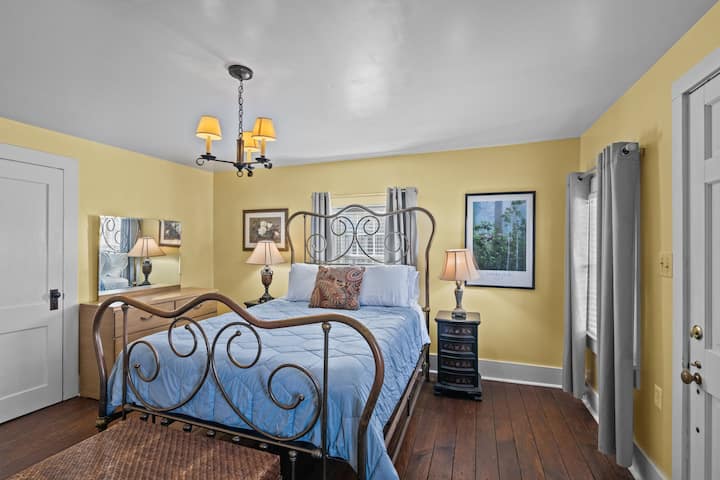 เสน่ห์สไตล์วินเทจมาบรรจบกับความอบอุ่นทันสมัยในห้องนอนชั้นล่างของบ้านประวัติศาสตร์ที่มีผนังสีเหลืองสดใสและเตาผิงตกแต่งแปลกตาเป็นเวทีสำหรับความเงียบสงบเหนือกาลเวลา