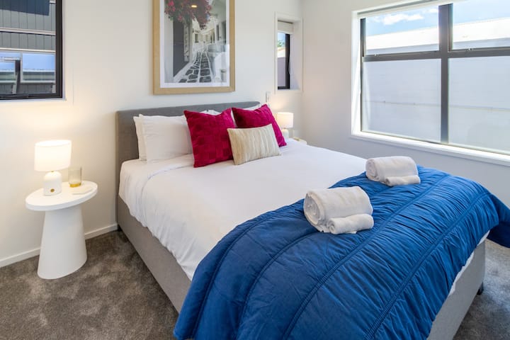 ห้องนอนกว้างขวางพร้อมเตียงควีนไซส์โคมไฟข้างเตียงและหมอน