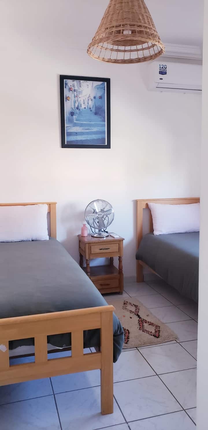 Chambre confortable avec deux lits simples, climatisation et décoration épurée, idéale pour amis ou enfants souhaitant partager la même chambre tout en gardant leur espace.