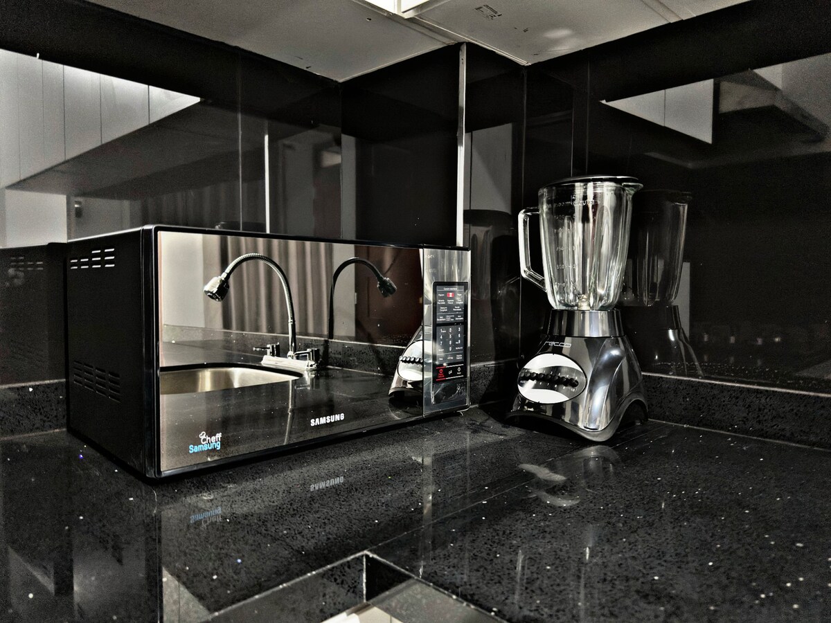A modern kitchen countertop features a microwave and a blender, both positioned on a glossy black surface. The sleek appliances are complemented by a stylish kitchen sink with a faucet, creating a functional cooking area.