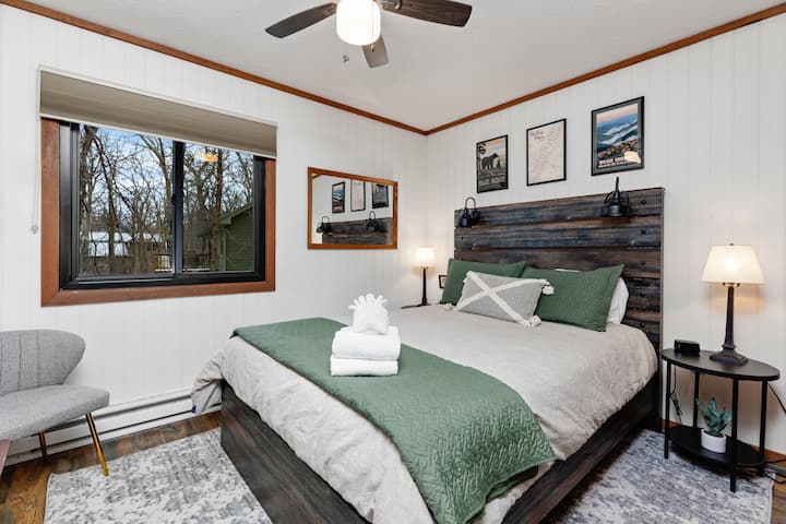 Dormitorio queen con cama tamaño queen, televisión de 55 pulgadas con todos los canales de streaming. Ventana con vistas al bosque con sombra de privacidad, ventilador de techo y enchufes USB.