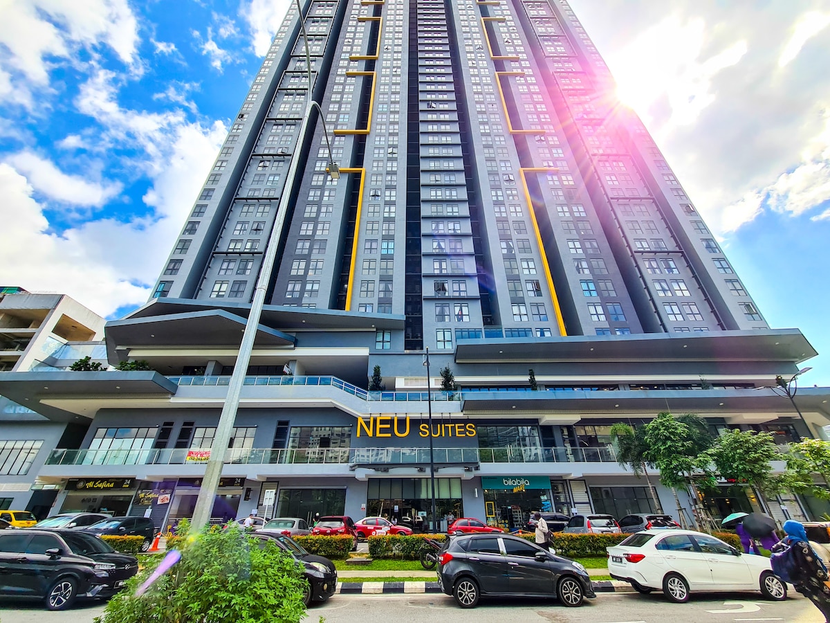 A modern high-rise building is prominently showcased, featuring a sleek glass facade and vibrant accents. The ground level includes a spacious lobby with retail establishments, while cars are parked along the street, indicating a bustling environment. Bright clouds reflect sunlight, enhancing the contemporary appeal.