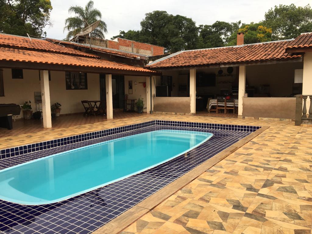 A private pool is surrounded by a tiled patio, featuring a rectangular shape with a blue interior. Nearby, an open courtyard presents covered seating areas under terracotta roofs, with wooden furniture positioned around the space. Lush greenery is visible in the background.