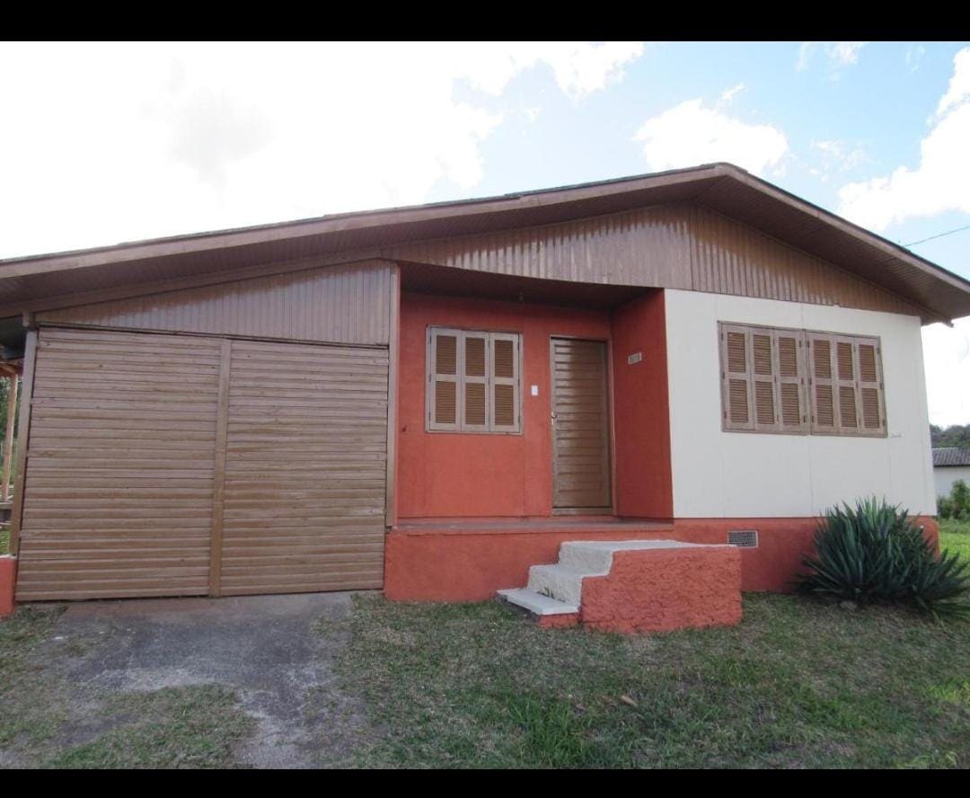 A spacious house is shown, with a blend of wood and vibrant exterior colors. The entrance features a set of wooden doors flanked by large windows. A short staircase leads up to the front door, surrounded by a grassy area and low landscaping.