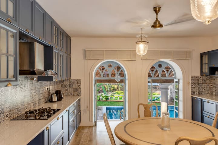 ✨This charming kitchen blends navy cabinetry, patterned tiles, and arched windows that frame a stunning view of the pool and garden✨