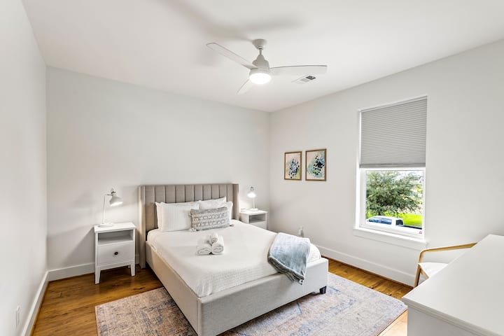 - Стилска брачна спална соба со штица за глава, удобна постелнина и меки неутрални тонови
- Две соодветни ноќни масички и модерен тавански вентилатор носат рамнотежа и удобност
- Големиот прозорец со сенка пропушта мека дневна светлина или целосна приватност кога е потребно