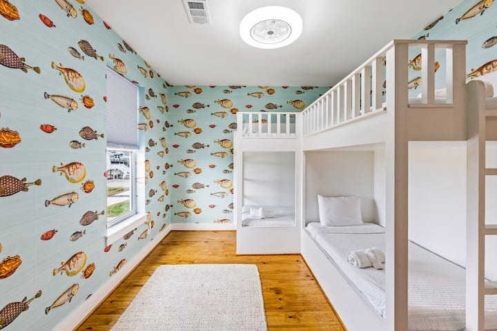 - Светла и разиграна соба на спрат со тапети со океанска тематика и свежи бели кревети
- Два двокреветни кревета создаваат забавен, удобен простор совршен за млади гости
- Природната светлина и топлите дрвени подови го балансираат веселиот и динамичен дизајн

