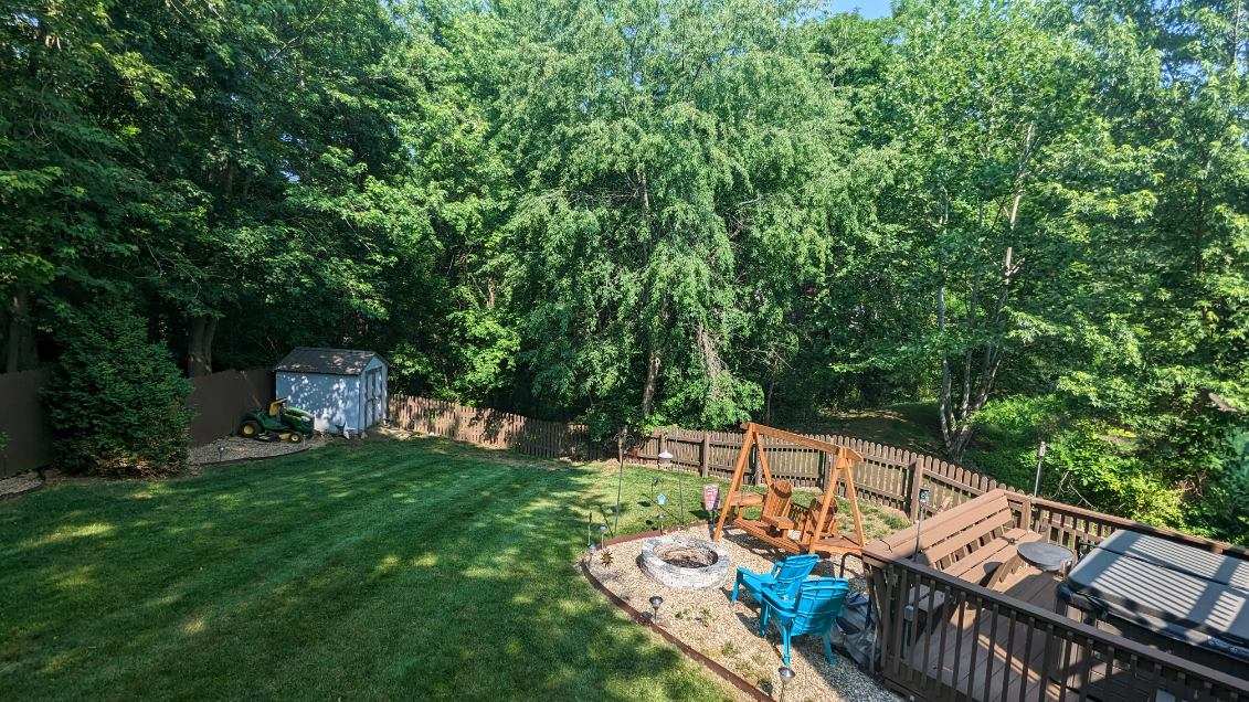 A spacious backyard setting is surrounded by tall trees, providing a natural privacy screen. A wooden deck is visible, accompanied by a hot tub and a fire pit area. A swing set adds a playful touch to the well-maintained lawn, which features neatly trimmed grass.
