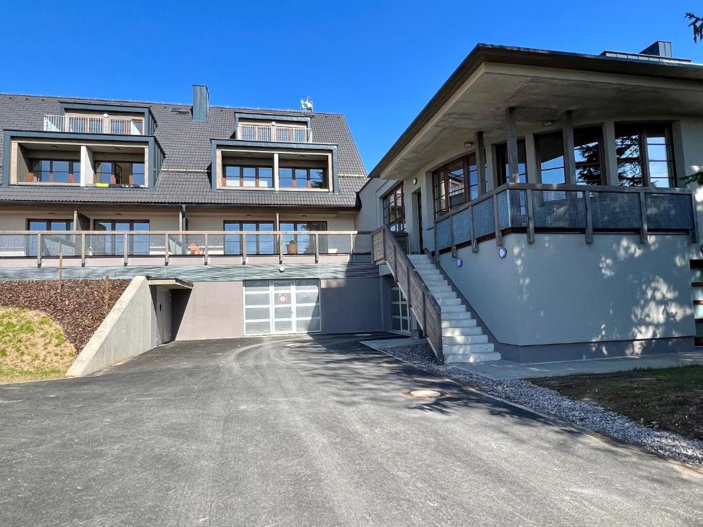 The exterior view showcases two distinct structures, with a modern building featuring multiple balconies and large windows. A spacious driveway leads to a garage, while steps ascend beside a well-lit entrance, highlighting an inviting outdoor area.