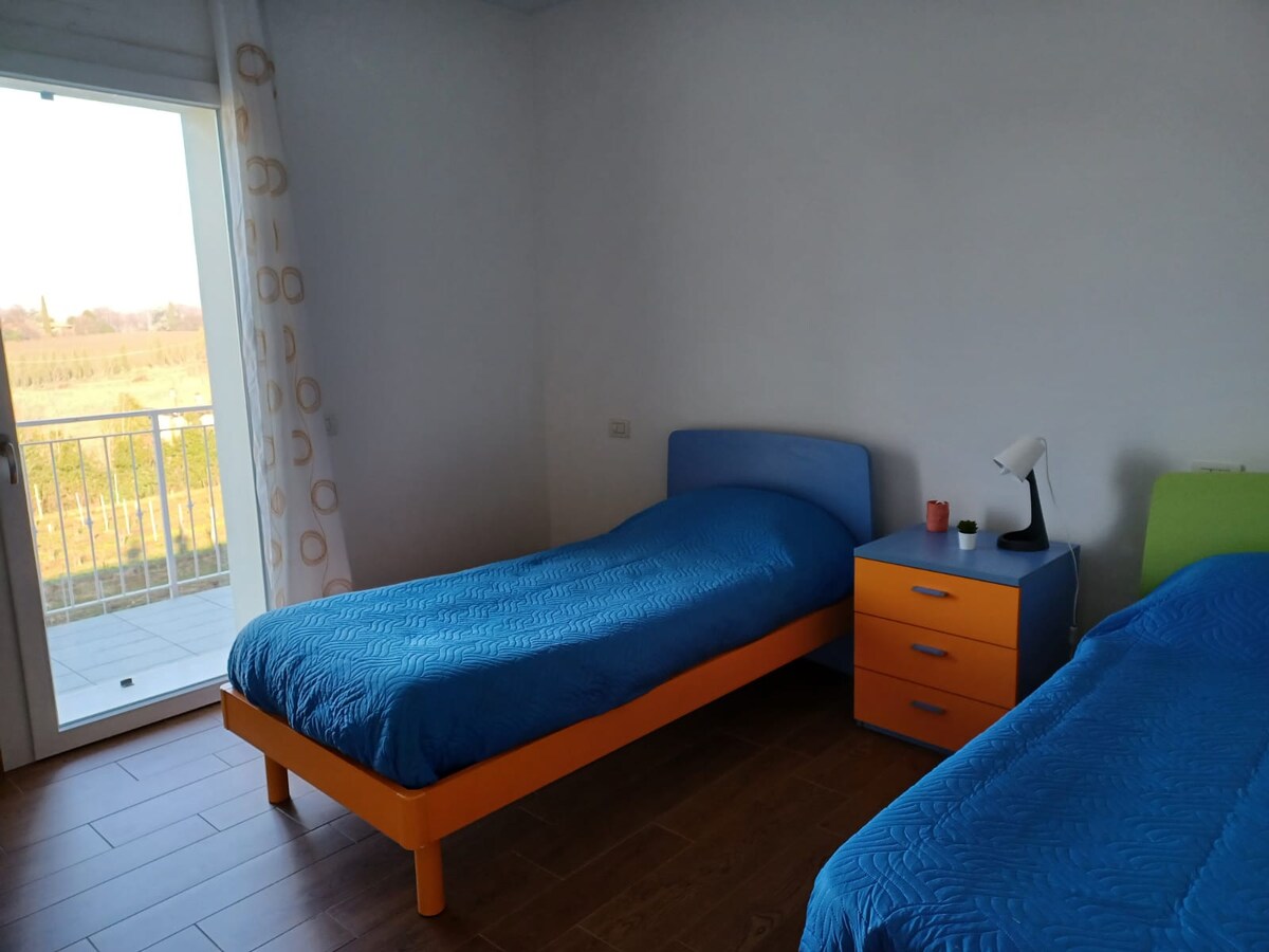 Phòng ngủ với 2 giường, bàn cạnh giường. Từ cửa sổ, bạn có thể ra ban công nhìn ra vườn nho và hoàng hôn