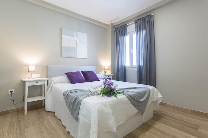 Glavna spavaća soba kombinira udobnost i minimalistički stil, s paletom mekih boja koja vas poziva na odmor. Krevet s bijelom posteljinom i detaljima u ljubičastoj boji, a apstraktna umjetnička djela prostoru daju sofisticiranu notu