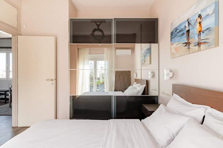 Un dormitorio acogedor con un cama grande, puertas de armario con espejos que reflejan un cuadro y vistas a una habitación contigua con balcón.