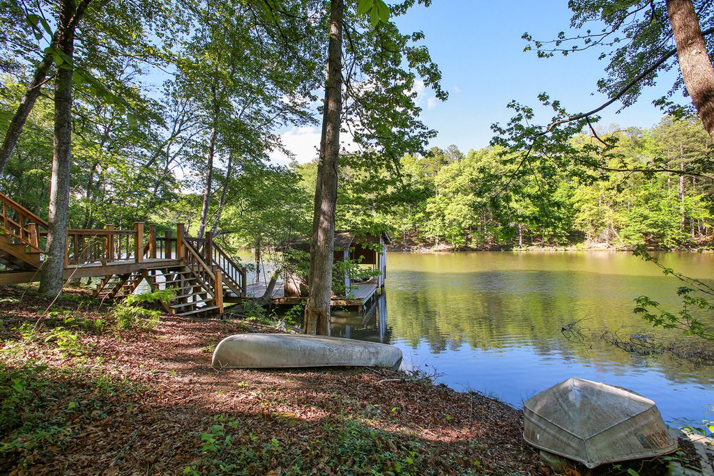 A serene lakeside scene is shown, featuring gentle water surrounded by lush greenery. A wooden staircase leads down to the water's edge, with boats resting on the shore, highlighting easy access to recreational activities.