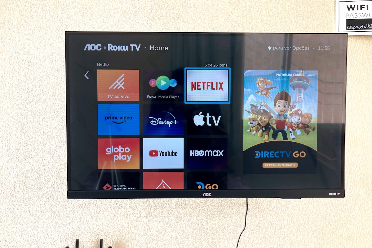 A wall-mounted smart TV displays various streaming service options, including Netflix and Disney+. The screen is oriented horizontally, providing easy access to entertainment choices. A nearby sign displaying WiFi password is also visible, positioned in the upper right corner.