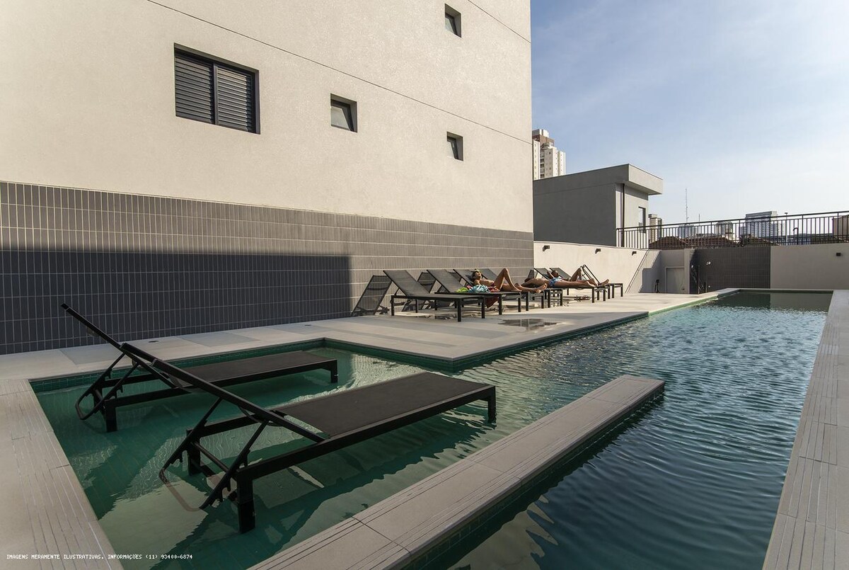 A modern outdoor pool area is featured, showcasing a sleek design with lounge chairs arranged around the water. The pool's surface reflects the clear sky, while shaded areas provide spaces for relaxation. A pool deck extends alongside, enhancing the overall layout.