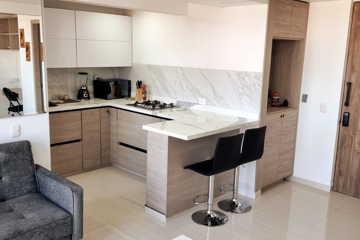 A modern kitchen is equipped with sleek cabinetry and a marble countertop. Two high-backed black stools are positioned at a small island, inviting casual dining. A coffee maker and other kitchen essentials are neatly arranged, enhancing functionality.