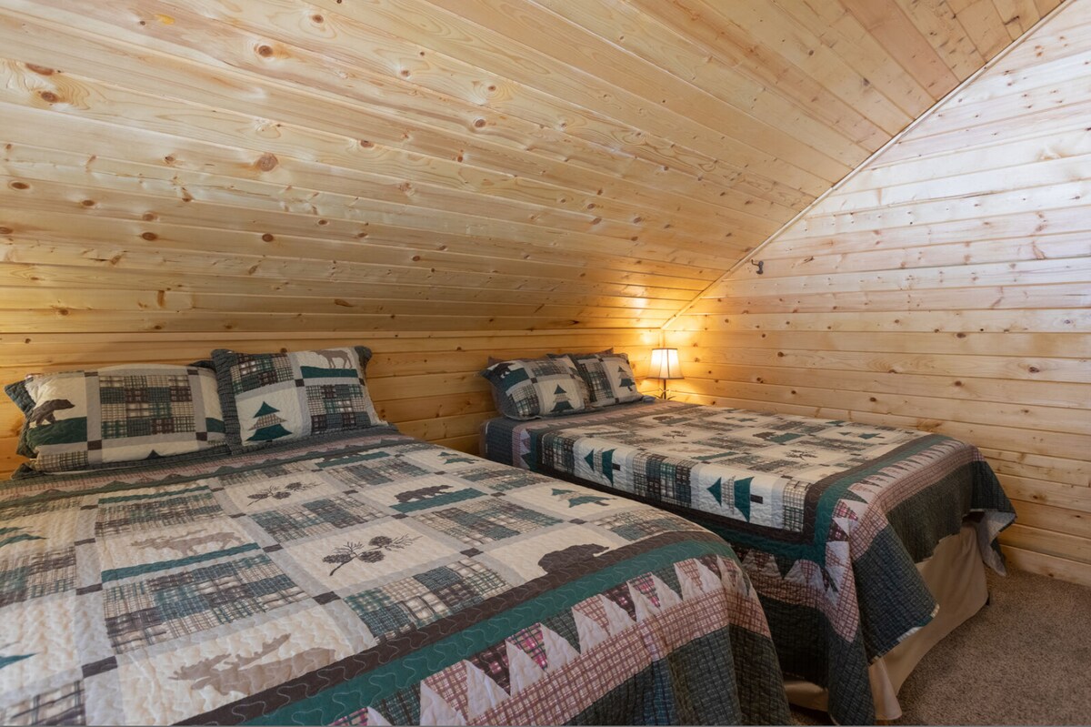 Spavaća soba na katu s dva bračna kreveta i toplim drvenim oblogama koja nudi jednostavan prostor za spavanje. 