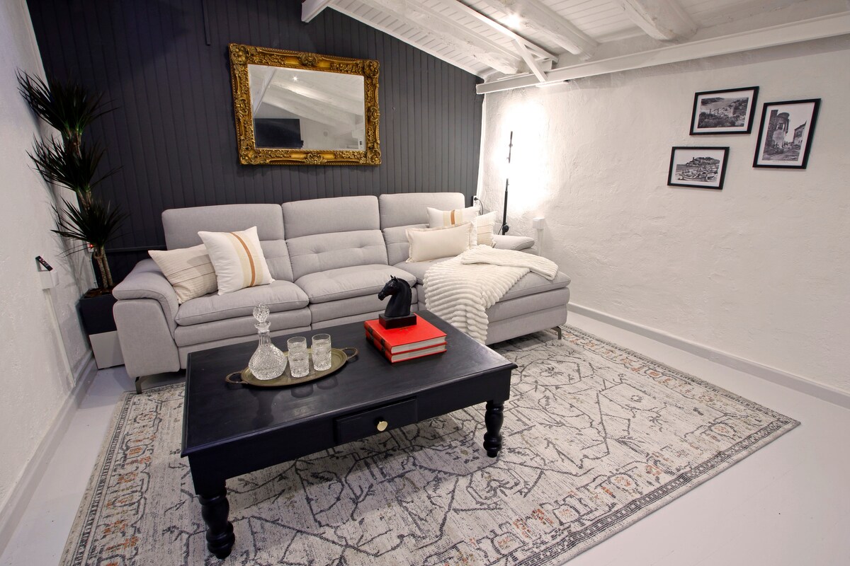 A welcoming living area features a light gray sofa with decorative pillows, positioned in front of a stylish black coffee table. A decorative area rug adds warmth, while framed artwork and a large mirror enhance the spaciousness. Soft lighting contributes to a cozy ambiance.