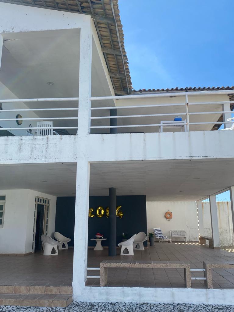 The exterior of the house showcases a two-level structure, featuring a spacious terrace with white seating and a decorative wall. Large windows allow natural light to fill the area, while a covered porch offers shelter from the sun.