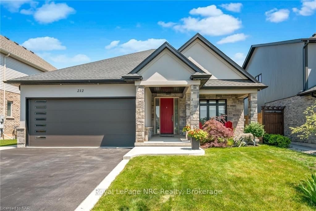 The exterior of the bungalow features a stone façade and a contemporary design. A welcoming red door stands at the entrance, complemented by landscaped greenery and colorful plants. The driveway provides ample parking space, while a two-car garage is visible on the left.