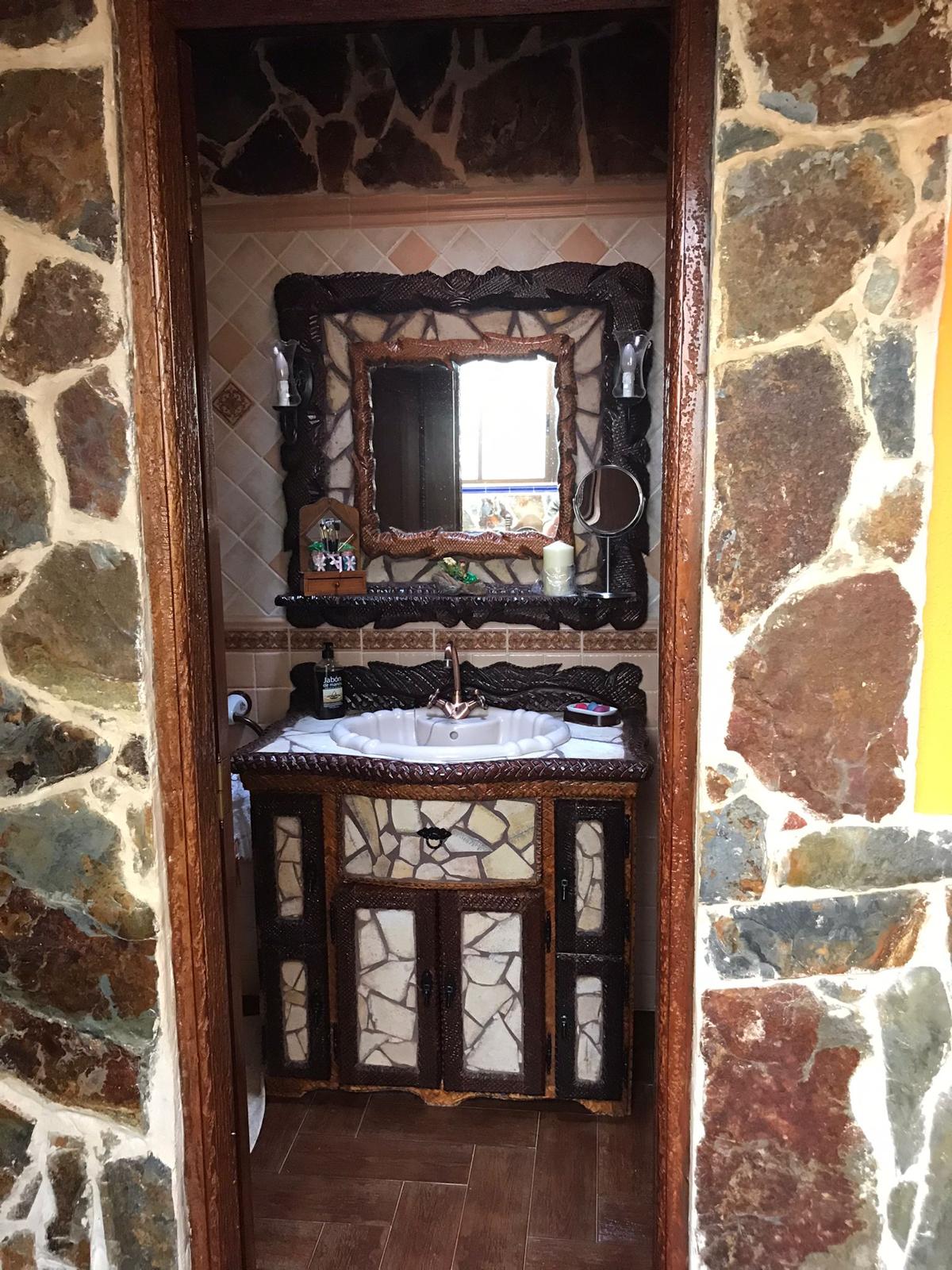 The bathroom features rustic stone walls and a unique wooden vanity with a marble countertop. A mirror is mounted above the sink, reflecting natural light. Decorative elements on the shelves add character, creating a cozy and functional space.
