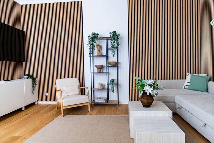 Una acogedora sala de estar con sofá, almohadas suaves y luz natural de grandes ventanales, perfecta para una estancia relajante y agradable. 