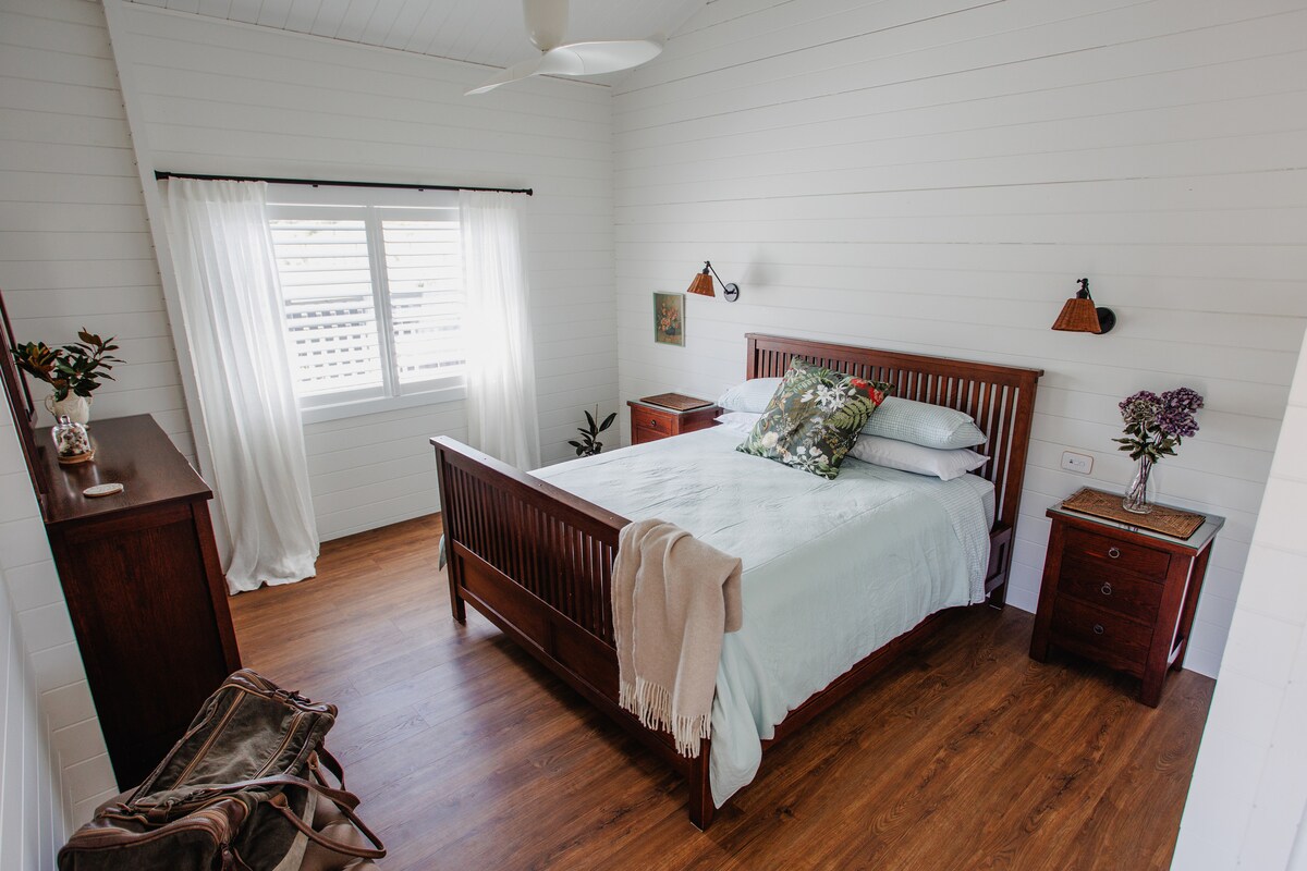 Spacious bedroom with high ceilings, superior king size bed, quality linen, ceiling fan, wardrobe, iron, drawers for clothing, bedside lights, and usb chargers.