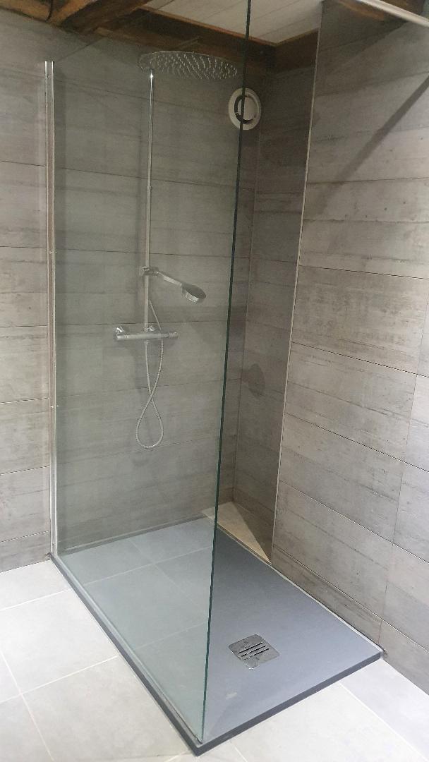 A modern walk-in shower is enclosed with clear glass panels. The sleek stone walls are complemented by a spacious shower base. A rain showerhead and handheld fixture are mounted on a minimalist chrome fixture, providing a contemporary look and functionality.
